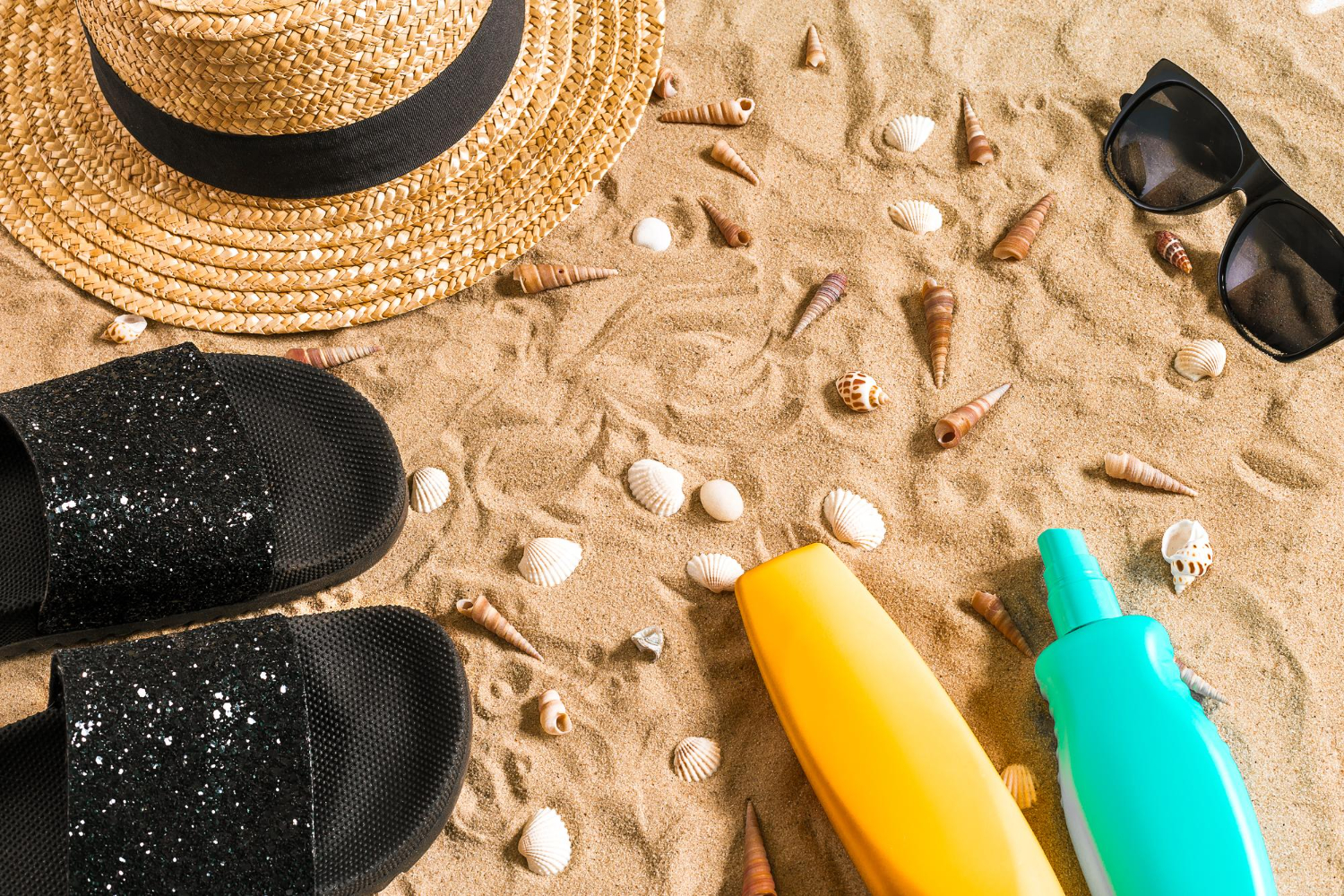Sun screen, sun glasses, straw hat and flip flops on the beach.
